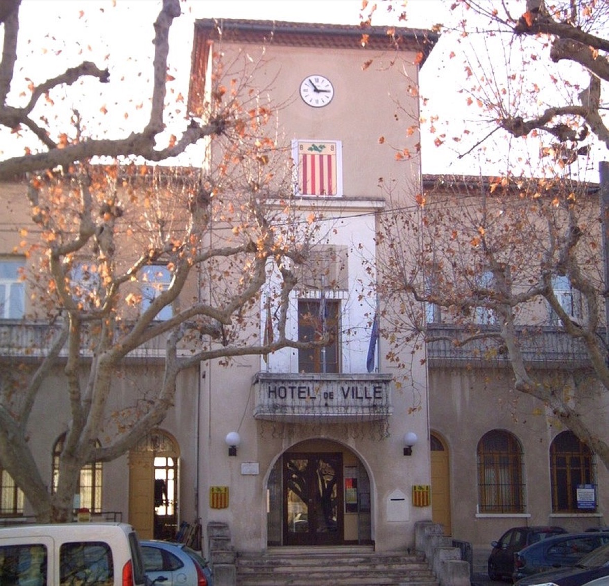 Façade de l'hôtel de ville avec son horloge, derrière les platanes de la place